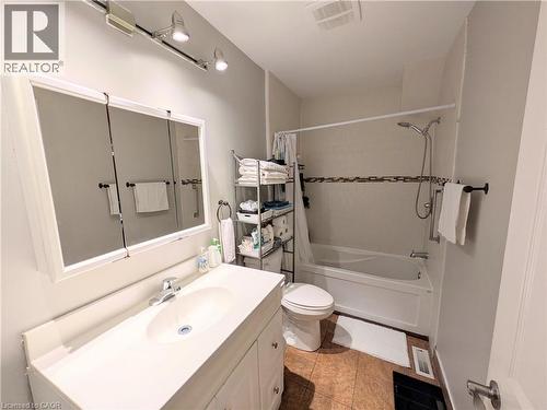 Bathroom featuring a white vanity with integrated sink, tri-panel mirrored medicine cabinet, track lighting, and a bathtub with a tiled surround - 7 Campbell Avenue, Hamilton, ON - Indoor Photo Showing Bathroom