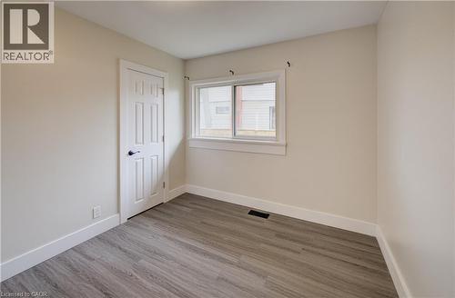 Neutral-toned room featuring light gray wood-finish flooring, a white six-panel door with matte black hardware, and a window with white trim - 361 Prospect Avenue, Kitchener, ON - Indoor Photo Showing Other Room