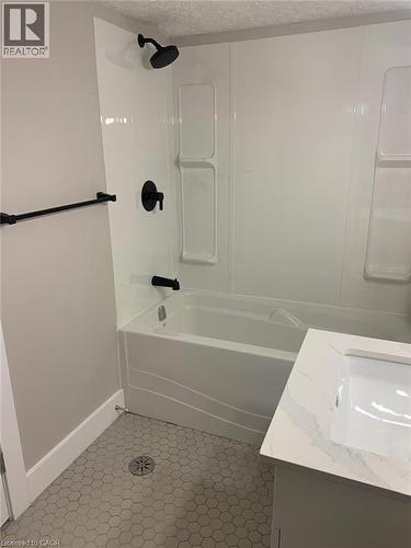 Bathroom featuring a white bathtub, integrated shower surround, matte black fixtures, grey hexagonal floor tiles, and a vanity with an integrated white sink and a white countertop - 361 Prospect Avenue, Kitchener, ON - Indoor Photo Showing Bathroom