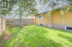 Fenced backyard featuring a mature tree, a manicured lawn, and a light-colored brick exterior - 