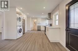 Open-concept kitchen featuring wood-finish flooring, white cabinetry with contemporary hardware, light-toned countertops, and a white subway tile backsplash - 