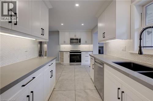 Galley kitchen featuring white cabinetry, light gray countertops, stainless steel appliances, and a herringbone tile backsplash - 244 Royal Street, Waterloo, ON - Indoor Photo Showing Kitchen With Double Sink