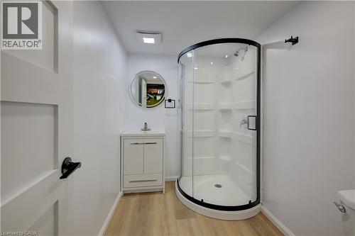 Curved glass shower enclosure with black trim, vanity with integrated sink, wood-finish flooring, and a circular mirror - 244 Royal Street, Waterloo, ON - Indoor Photo Showing Bathroom