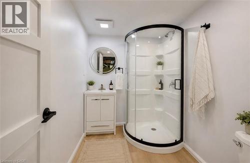 Curved glass shower enclosure with matte black trim, white vanity with integrated sink, circular mirror, and wood-finish flooring - 244 Royal Street, Waterloo, ON - Indoor Photo Showing Bathroom
