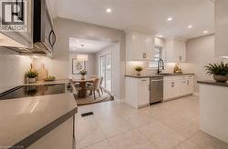 White shaker cabinetry, stainless steel appliances, tile flooring, recessed lighting, and a herringbone tile backsplash - 