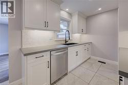 White shaker cabinetry, herringbone tile backsplash, under-cabinet lighting, dark countertop, and large format tile flooring - 