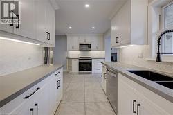 Galley kitchen featuring white cabinetry, light gray countertops, stainless steel appliances, and a herringbone tile backsplash - 