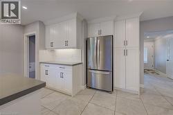 White shaker cabinetry, stainless steel French door refrigerator, light gray countertops, white geometric tile backsplash, and light gray tile flooring - 