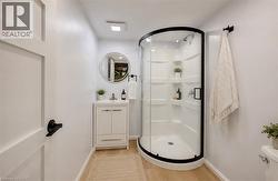 Curved glass shower enclosure with matte black trim, white vanity with integrated sink, circular mirror, and wood-finish flooring - 