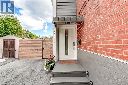 Entry with red brick and gray siding, white door with vertical glass insert, covered porch with steps, and a wood-slat fence - 2488 Brookhurst Road, Mississauga, ON - Outdoor With Exterior
