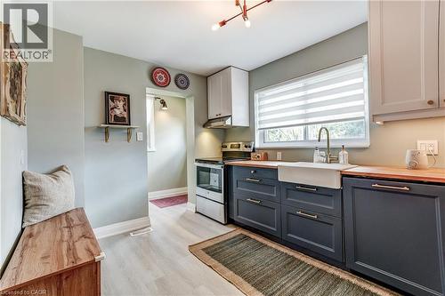Kitchen featuring light wood-finish flooring, white upper cabinetry, dark lower cabinetry, wood countertops, and a white farmhouse sink with a gooseneck faucet - 2488 Brookhurst Road, Mississauga, ON - Indoor Photo Showing Kitchen