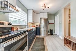 Kitchen featuring light wood-finish flooring, two-tone cabinetry, a farmhouse-style sink, and stainless steel appliances - 