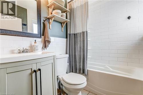 White subway tile tub surround, built-in bathtub, light-colored vanity with double doors and dark hardware, single basin sink, and wood-toned open shelving - 2488 Brookhurst Road, Mississauga, ON - Indoor Photo Showing Bathroom