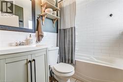 White subway tile tub surround, built-in bathtub, light-colored vanity with double doors and dark hardware, single basin sink, and wood-toned open shelving - 