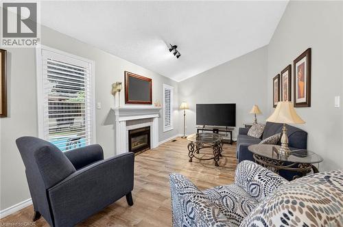 Vaulted ceiling, wood-finish flooring, white fireplace surround, fireplace insert, and window with plantation shutters - 43 Liam Drive, Ancaster, ON - Indoor Photo Showing Living Room With Fireplace