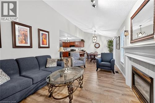 Vaulted ceiling, wood-finish flooring, fireplace with white mantel, built-in kitchen cabinetry, and pendant light fixtures - 43 Liam Drive, Ancaster, ON - Indoor Photo Showing Living Room With Fireplace