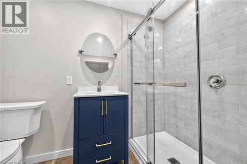 Modern bathroom featuring a glass-enclosed shower with subway tile surround, a dark blue vanity with gold-tone hardware, a white countertop, and a contemporary round mirror - 43 Liam Drive, Ancaster, ON - Indoor Photo Showing Bathroom