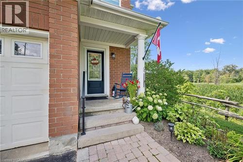 Brick exterior featuring a covered porch with white columns, a dark entry door with decorative glass, and a paved walkway - 439 Beaver Creek Road, Waterloo, ON - Outdoor With Deck Patio Veranda With Exterior