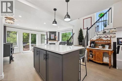Central island with a light-toned countertop, wood-finish flooring, sliding glass patio doors, built-in fireplace, and a staircase with an iron railing - 439 Beaver Creek Road, Waterloo, ON - Indoor Photo Showing Kitchen