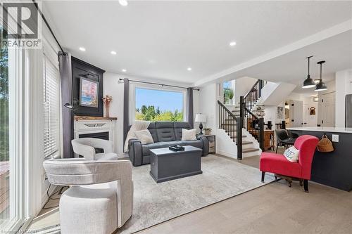 Recessed ceiling lighting, wood-finish flooring, built-in fireplace with mantel, staircase with dark wood-finish handrail and black balusters, and a built-in kitchen island with pendant lighting - 439 Beaver Creek Road, Waterloo, ON - Indoor Photo Showing Living Room