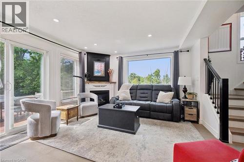 Recessed lighting, fireplace with mantel, large picture window, glass sliding door, and wood-finish stairs with black railings - 439 Beaver Creek Road, Waterloo, ON - Indoor Photo Showing Living Room With Fireplace