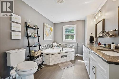 Corner soaking tub with mosaic tile surround, wood-finish flooring, dual vanity with undermount sinks, and a window providing natural light - 439 Beaver Creek Road, Waterloo, ON - Indoor Photo Showing Bathroom
