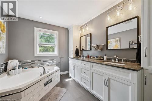 Dual sink vanity with stone-finish countertop, white cabinetry with silver hardware, large soaking tub with subway tile surround, and wood-finish flooring - 439 Beaver Creek Road, Waterloo, ON - Indoor Photo Showing Bathroom