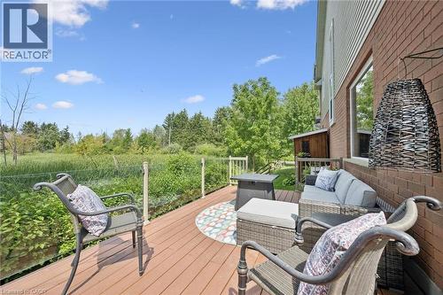 Expansive wood-finish deck with brick exterior, featuring a glass panel railing and open green space - 439 Beaver Creek Road, Waterloo, ON - Outdoor With Deck Patio Veranda With Exterior