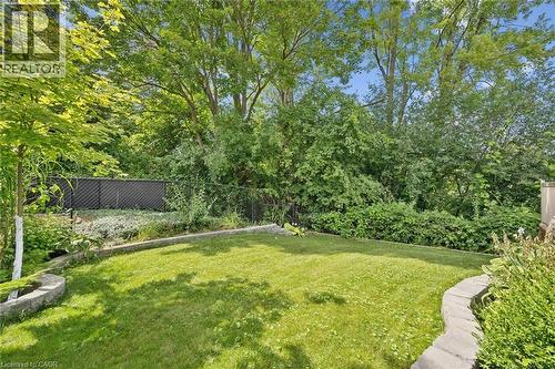 Manicured lawn with a stone-edged garden bed, surrounded by mature trees and a dark privacy fence - 439 Beaver Creek Road, Waterloo, ON - Outdoor