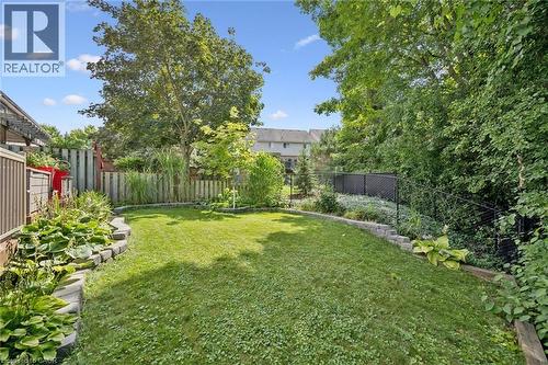 Expansive backyard featuring a manicured lawn, tiered landscaping with stone block retaining walls, mature trees, and privacy fencing - 439 Beaver Creek Road, Waterloo, ON - Outdoor