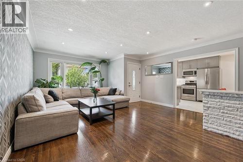 Rich wood flooring, modern recessed lighting, textured accent wall, white crown molding, and a kitchen pass-through with stone-look detailing - 49 East Street, Cambridge, ON - Indoor Photo Showing Living Room