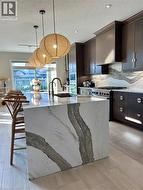 Kitchen featuring a waterfall island with stone-finish countertop, dark wood-finish cabinetry, and a gas range - 