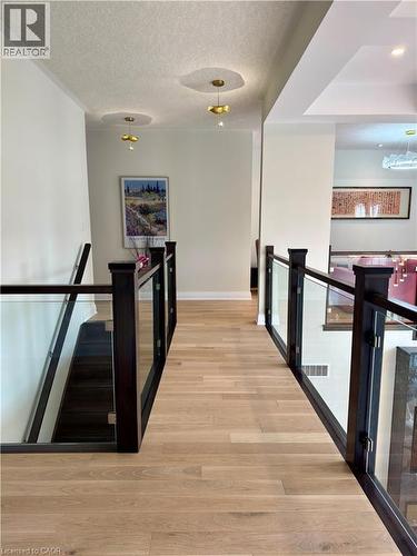 Hardwood flooring, dark wood newel posts, glass railings, and modern pendant lighting - 923 Eaglecrest Court, Kitchener, ON - Indoor Photo Showing Other Room