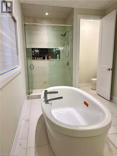 Freestanding soaking tub with chrome fixtures, glass-enclosed shower with tile surround, built-in shower niche with herringbone tile accent, and large format tile flooring - 923 Eaglecrest Court, Kitchener, ON - Indoor Photo Showing Bathroom