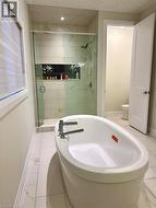 Freestanding soaking tub with chrome fixtures, glass-enclosed shower with tile surround, built-in shower niche with herringbone tile accent, and large format tile flooring - 