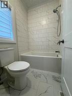 Bathtub and shower combination with subway tile surround, tile flooring, and a white framed window with blinds - 