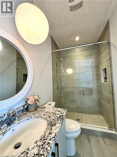 Walk-in shower with clear glass enclosure and tiled walls, vanity with a white basin and speckled countertop, and wood-finish flooring - 923 Eaglecrest Court, Kitchener, ON - Indoor Photo Showing Bathroom