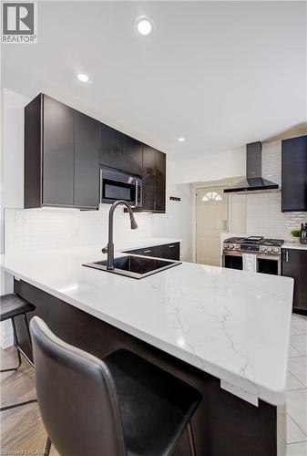 Modern kitchen featuring a large island with a composite countertop, an undermount sink with a matte black faucet, recessed lighting, and dark flat-panel cabinetry - 34 St Clair Avenue, Kitchener, ON - Indoor Photo Showing Kitchen With Double Sink With Upgraded Kitchen