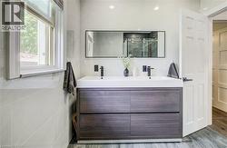 Dual sink vanity with wood-finish cabinetry, matte black fixtures, and a framed mirror - 