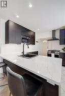 Modern kitchen featuring a large island with a composite countertop, an undermount sink with a matte black faucet, recessed lighting, and dark flat-panel cabinetry - 