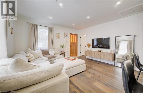 Spacious living area featuring a curved sectional arrangement, wood-finish flooring throughout, recessed ceiling lighting, and a wall-mounted flat-screen television - 34 St Clair Avenue, Kitchener, ON - Indoor Photo Showing Living Room