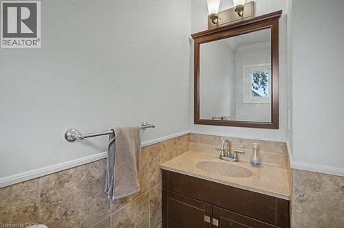 Wood-framed mirror, dual sconce lighting, vanity with integrated sink, stone countertop, and tile wainscoting - 2050 Upper Middle Road Unit# 164, Burlington, ON - Indoor Photo Showing Bathroom