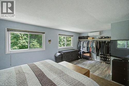 Spacious room featuring two windows, wood-finish flooring, a built-in closet system with shelving, and a wall-mounted climate control unit - 2050 Upper Middle Road Unit# 164, Burlington, ON - Indoor Photo Showing Bedroom
