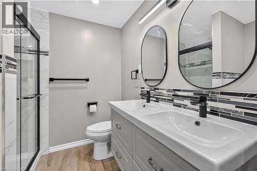 Dual white basin vanity with matte black fixtures, framed by two oval mirrors and a horizontal tile backsplash - 66 Summercrest Drive Unit# 3, Hamilton, ON - Indoor Photo Showing Bathroom