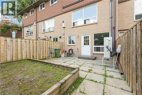 Rear exterior featuring a brick facade, white door with glass panels, large windows, and a paved patio area - 66 Summercrest Drive Unit# 3, Hamilton, ON - Outdoor With Exterior