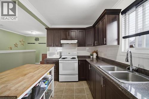 Dark wood-finish cabinetry with crown molding, white tile backsplash, and a double basin stainless steel sink - 22 Delena Avenue N, Hamilton, ON - Indoor Photo Showing Kitchen With Double Sink