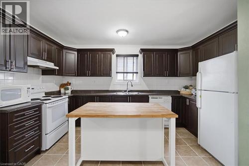 Kitchen featuring dark wood-finish cabinetry, white subway tile backsplash, a center island with a wood-finish top, and tile flooring - 22 Delena Avenue N, Hamilton, ON - Indoor Photo Showing Kitchen With Double Sink