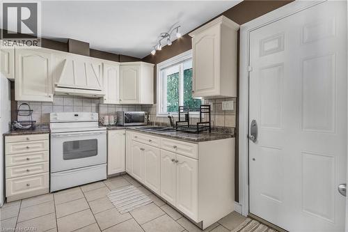 Light-toned cabinetry with decorative molding, solid surface countertops, tiled flooring, built-in range hood, and a window with natural light - 185 Burlington Street, London, ON - Indoor Photo Showing Kitchen With Double Sink