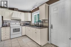 Light-toned cabinetry with decorative molding, solid surface countertops, tiled flooring, built-in range hood, and a window with natural light - 
