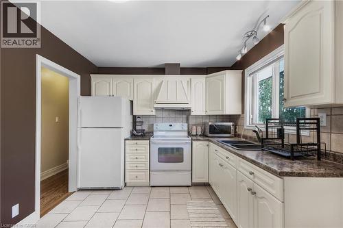 White cabinetry with integrated range hood, tile backsplash, laminate countertops, and ceramic tile flooring - 185 Burlington Street, London, ON - Indoor Photo Showing Kitchen With Double Sink